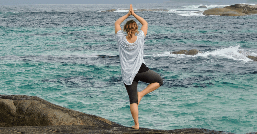 Woman meditating on a rock by the ocean