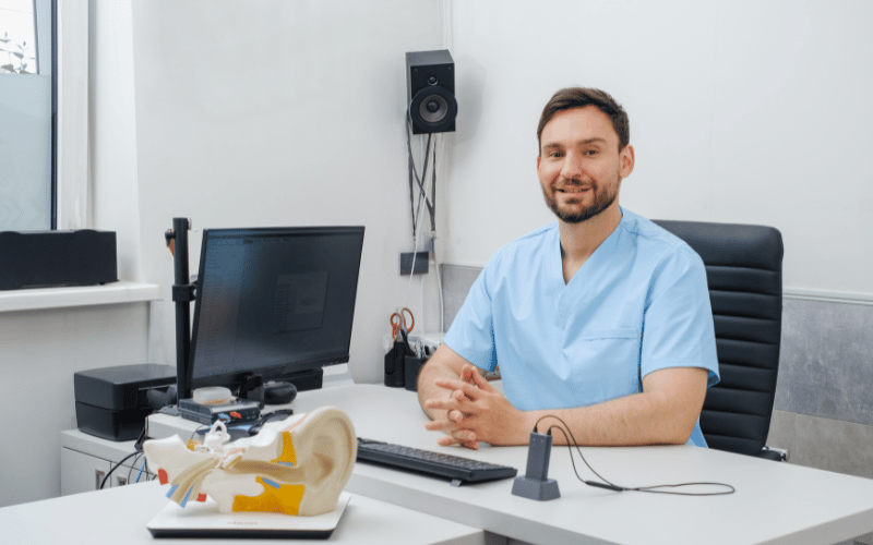 Audiologist sitting at his desk with a model of an ear in front of him 