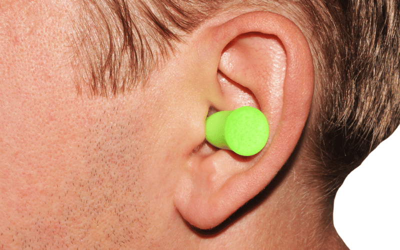 Person with a green foam earplug in their ear