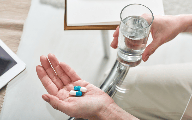 Person holding pills in one hand with a glass of water in the other hand